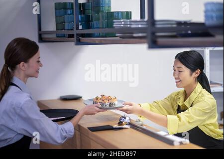 Serveuse asiatique servant des sushis au client Banque D'Images