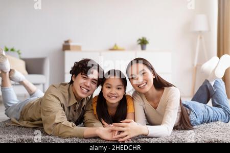 Joyeuse femme asiatique millénaire, gars et fille de l'adolescence se trouvent sur le sol et tiennent les mains dans l'intérieur de la salle de séjour Banque D'Images