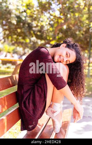 Jeune ballerine souriante en robe noire assise sur un banc de parc Banque D'Images