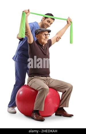 Physiothérapeute travaillant avec un homme âgé assis sur une balle d'exercice et utilisant une bande d'étirement isolée sur fond blanc Banque D'Images