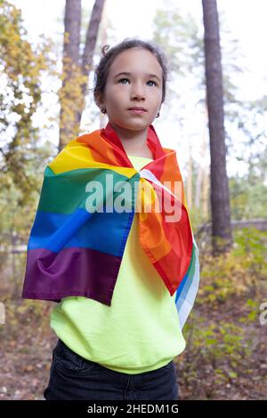 Petite fille caucasienne avec cheveux bouclés tenant un drapeau arc-en-ciel. concept lgbtq. Banque D'Images