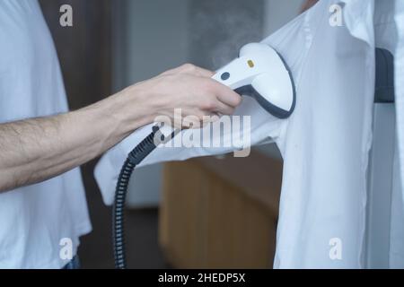Prise de vue courte d'un homme à l'aide d'un défroisseur électrique tout en cuisant une chemise classique à la maison Banque D'Images