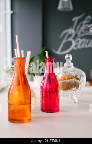 Bouteilles en verre colorées avec pailles en papier pour boissons ou cocktails et un bol de biscuits en arrière-plan Banque D'Images