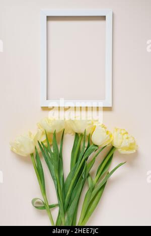 Bouquet de tulipes de printemps jaunes sur la table, à côté d'un cadre photo blanc vide avec espace de copie.Pose à plat Banque D'Images