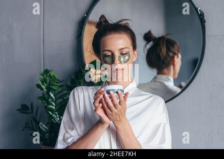 Femme tenant un pot de timbres d'oeil tout en se tenant dans la salle de bains. Banque D'Images