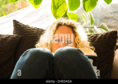 femme blonde lisant confortablement un livre sur le canapé Banque D'Images