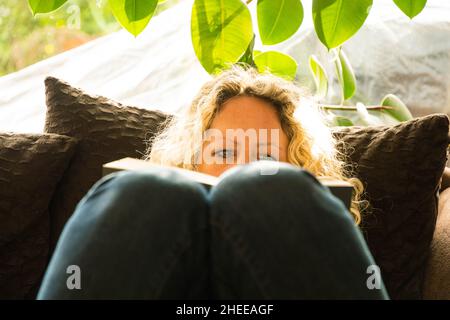 femme blonde lisant confortablement un livre sur le canapé Banque D'Images