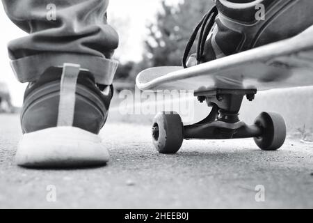 Gros plan de planche à roulettes et de pieds, photo stylisée rétro monochrome.Jeune skateboarder debout sur son skate. Banque D'Images