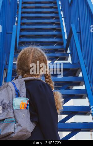 Une écolière regardant les escaliers...Concept école jours, date de début, étape suivante, échelle de carrière, le début de la voie. Fille dans un uniforme avec un bac Banque D'Images