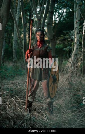 Corps complet de femme brave en costume viking debout avec lance et bouclier pour la reconstitution médiévale dans les bois Banque D'Images