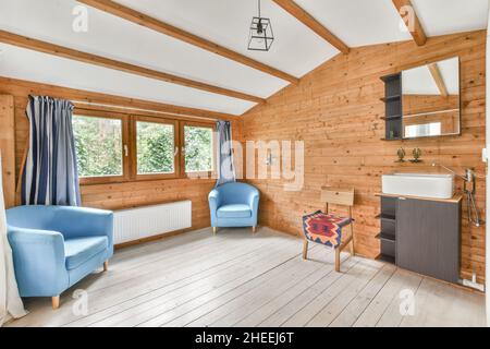 Intérieur de chambre spacieuse avec fauteuils confortables près de la fenêtre et miroir suspendu sur un mur en bois au-dessus du lavabo Banque D'Images