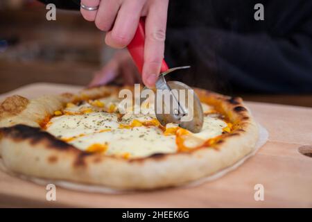 Crop-female Cutting savoureuse pizza cuite avec couteau tranchant servi sur planche à découper en bois à table dans la cuisine légère Banque D'Images