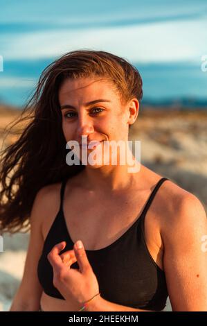 Femme positive attrayante brunette avec des cheveux longs et le port noir dessus regardant l'appareil photo dans la lumière du soleil Banque D'Images