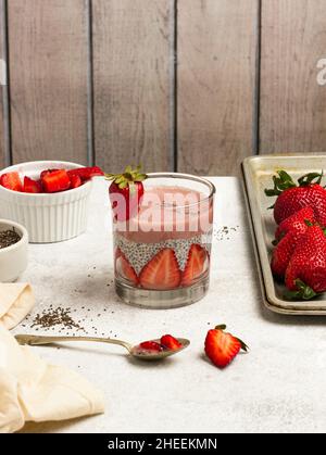 Délicieux pudding aux graines de chia et aux tranches de fraises fraîches placées sur la table à côté des ingrédients pour un petit déjeuner sain Banque D'Images