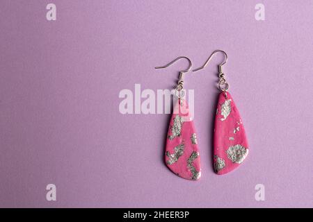 Boucles d'oreilles roses et argentées sur fond violet. Banque D'Images