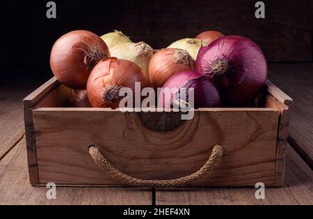 Oignons dans une ancienne boîte sur une table rustique en bois, ingrédients alimentaires Banque D'Images