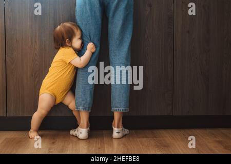 Babygirl se cachant derrière les jambes des mères dans la cuisine Banque D'Images