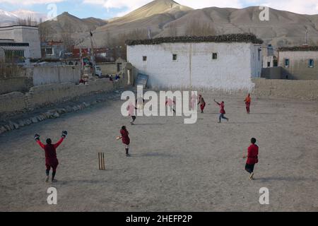 Photographie couleur de moines bouddhistes jouant à une partie de cricket sur une cour en terre battue, Lo Manthang, Mustang, Népal, Asie, 2011. Banque D'Images