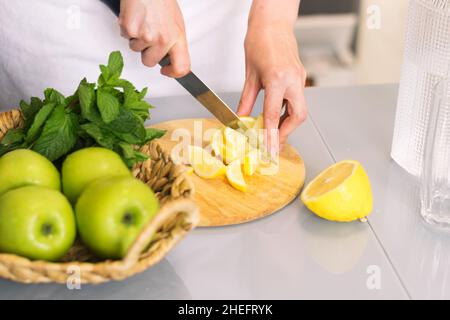 Femme faisant de la boisson de détox avec citron et menthe dans la cuisine à la maison.Eau revigorante rajeunissant citron, antioxydant. Banque D'Images