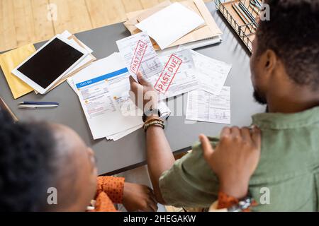 Femme africaine réconfortant jeune homme troublé regardant à travers les journaux financiers tout en étant assis à table Banque D'Images