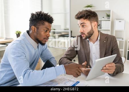 L'un des deux hommes d'affaires confiants expliquant les données en ligne à leurs collègues lors de discussions sur les points financiers lors de la réunion Banque D'Images