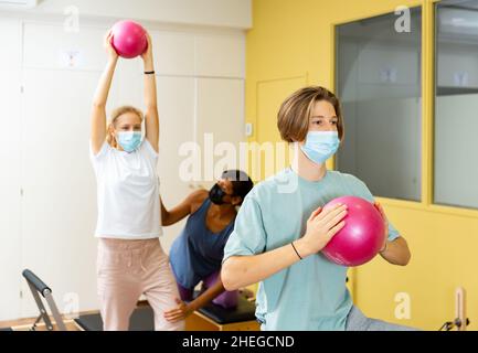 Adolescents dans les masques d'entraînement pilates dans la salle de gym avec entraîneur Banque D'Images