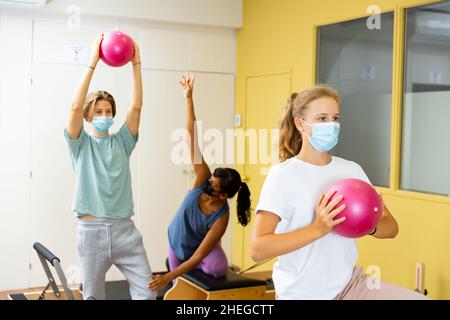 Adolescents dans les masques d'entraînement pilates dans la salle de gym avec entraîneur Banque D'Images