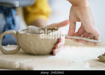 Un céramiste artisanal au travail utilise des outils pour créer une tasse faite à la main en studio.Gros plan des mains femelles potter Banque D'Images