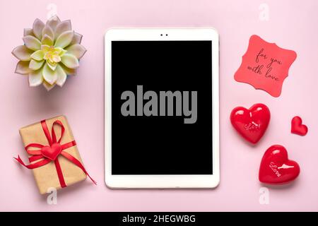 Tablette numérique pour choisir des cadeaux, faire l'achat, enveloppe, coeur rouge sur table rose vue du dessus plat Lay liste d'achats de vacances, bonne Saint-Valentin Banque D'Images