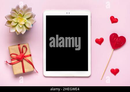 Tablette numérique pour choisir des cadeaux, faire l'achat, enveloppe, coeur rouge sur table rose vue du dessus plat Lay liste d'achats de vacances, bonne Saint-Valentin Banque D'Images