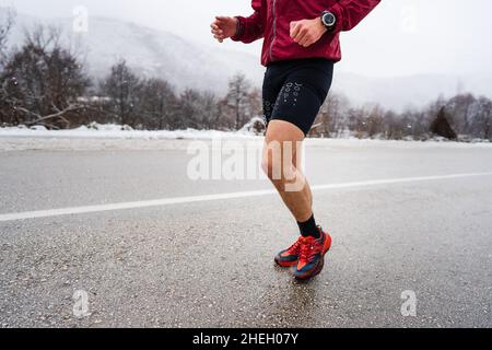Un homme caucasien adulte courant en hiver jour athlète masculin entraînement sur la route ouverte dans la nature avec la neige santé et le concept de forme physique personnes réelles Banque D'Images