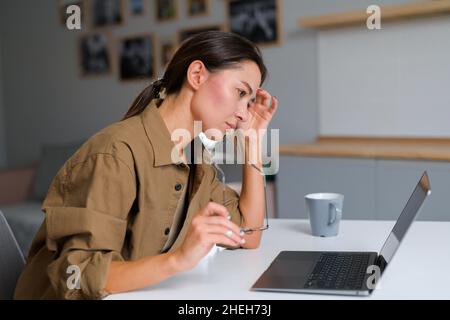 Inquiète femme asiatique travaillant à domicile, regardant l'écran de l'ordinateur portable avec désespoir.Une femme coréenne insatisfaite et multiraciale freelance ressent du stress et de l'épuisement, à la recherche d'un emploi Banque D'Images