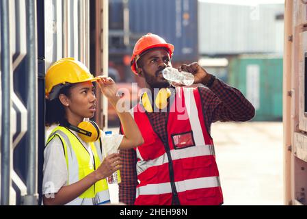 Homme et femme un technicien africain américain boit de l'eau et se repose après avoir travaillé dans une cour de conteneurs. Banque D'Images