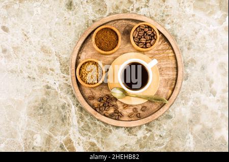 Plateau rond en bois avec une tasse de café foncé et divers types de café dans des mini-bols. Vue sur le dessus. Fond en marbre Banque D'Images