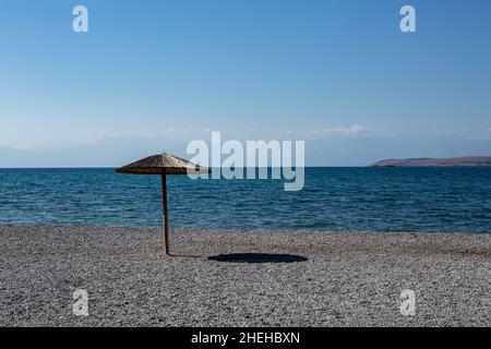 parapluie jetant une ombre sur une plage de galets déserte de personnes ciel bleu et mer bleue Banque D'Images