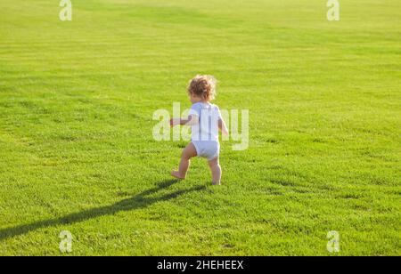 Vue arrière de bébé marchant dans le parc dans un pantalon de couches. Enfant en bonne santé. Banque D'Images
