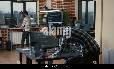 Codage par un développeur senior sur un ordinateur portable à un bureau avec écrans d'ordinateur analysant le code dans une agence logicielle.Programme compilant le langage de programmation avec l'équipe des algorithmes d'apprentissage machine innovants . Banque D'Images