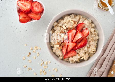 Porridge de flocons d'avoine avec tranches de fraises, amandes de noix et miel dans un bol pour la Saint-Valentin sur table grise.Concept pour un petit déjeuner ou un repas romantique.Haut Banque D'Images