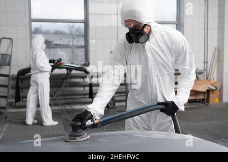 Workman en costume de noisette travaillant avec le cireuse de voiture dans le garage Banque D'Images