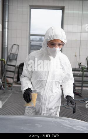 Femme de travail en costume de noisette tenant le papier de verre près de la voiture dans le garage Banque D'Images