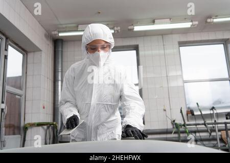 Femme de travail en costume de noisette tenant le papier de verre près de la voiture dans le garage Banque D'Images