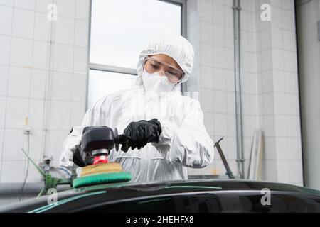 Workwoman en costume noisette et masque de protection voiture de polissage en service Banque D'Images