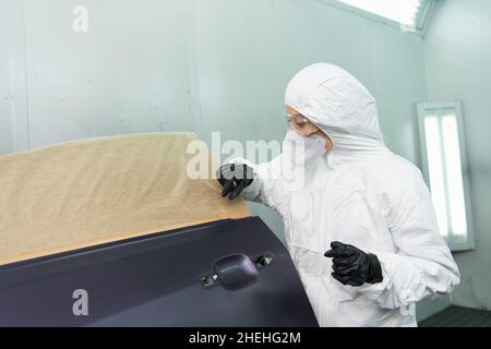 Femme de travail en costume de noisette travaillant avec pièce de voiture dans le garage Banque D'Images