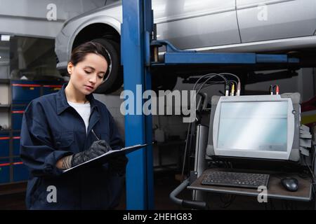 Workwoman écrivant sur le presse-papiers près de l'ordinateur et de la voiture en service Banque D'Images