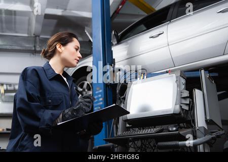 Vue latérale de l'écriture préewoman sur le presse-papiers près de l'ordinateur et de la voiture dans le garage Banque D'Images