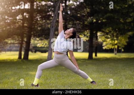 Jeune femme pratiquant le yoga dans un parc public au lever du soleil Banque D'Images