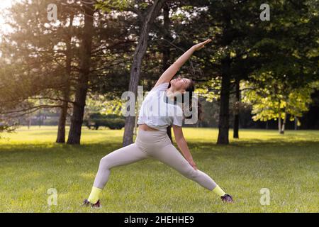 Jeune femme pratiquant le yoga dans un parc public au lever du soleil Banque D'Images