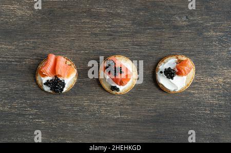 Trois crêpes blini avec caviar d'esturgeon noir et saumon sur une table en bois Banque D'Images