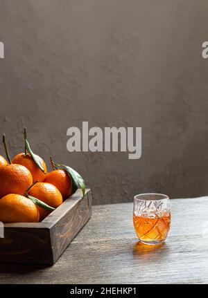 Une liqueur de mandarine et une boîte de mandarines fraîches sur table en bois, photo verticale avec espace de copie Banque D'Images