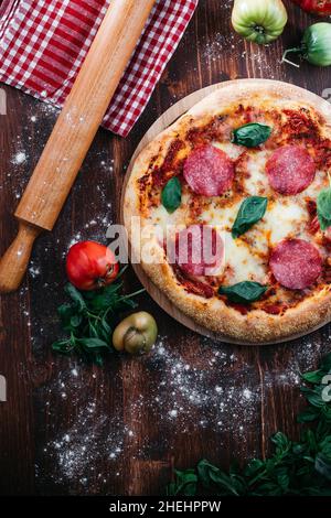 Pizza, traditionnelle et authentique avec mozzarella, pâte de tomate et basilic frais.Placé sur une planche de bois avec des ingrédients et une goupille élastique. Banque D'Images